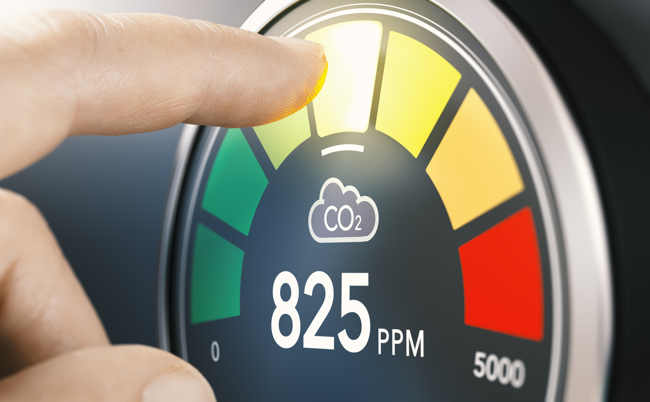 Finger touching digital screen of a CO2 monitor to measure indoor air quality and carbon dioxide concentration. Composite image between a hand photography and a 3D background.